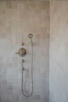 a shower head and hand held shower faucet in a white tiled bathroom area