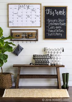 a wooden bench sitting in front of a wall with calendars and plants on it