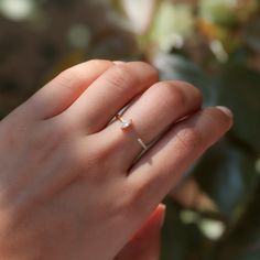 a woman's hand with a diamond ring on top of her finger and a plant in the background