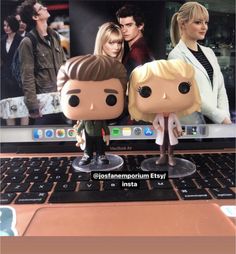 two figurines are sitting on top of a laptop computer, with the screen showing movies