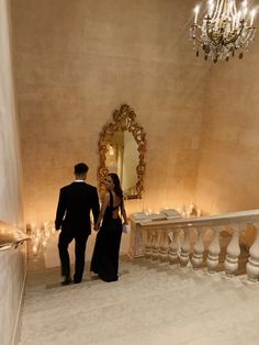 a man and woman are walking down the stairs in front of a chandelier