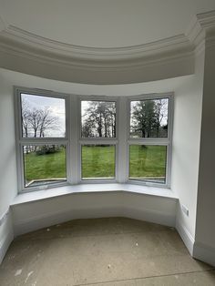 an empty corner room with three windows on the wall and grass in the window sill