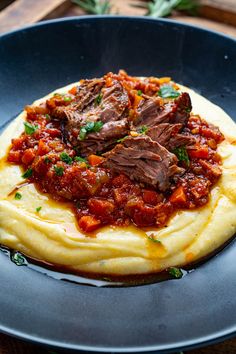 a blue plate topped with mashed potatoes covered in meat and sauce on top of a wooden table