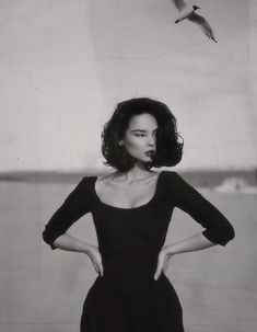 a black and white photo of a woman with her hands on her hips standing in front of a seagull