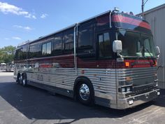 a silver and red bus parked in a lot next to a metal building on a sunny day