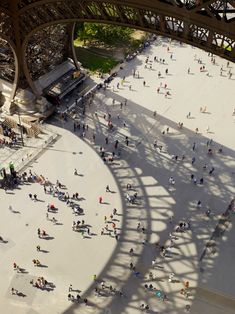 an aerial view of people walking around in the sun under a large metal structure with a long shadow on it