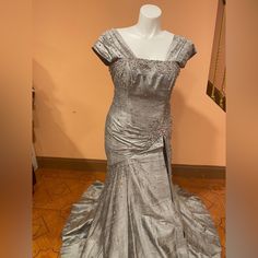 a dress on display in a room with wooden flooring and walls behind it is a mannequin wearing a silver gown