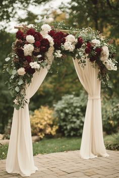 two white and red flowers are on top of the drapes for an outdoor ceremony