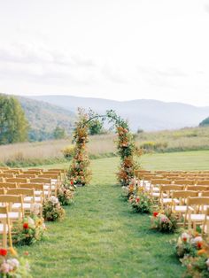 an outdoor ceremony set up with wooden chairs and flowers on the aisle, surrounded by greenery