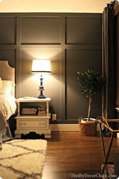 an image of a bedroom with gray walls and white furniture, including a lamp on the end table