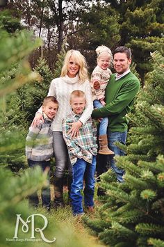 a family posing for a photo in the christmas tree farm with their two children and one adult