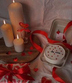 a table topped with candles and cake next to two plates covered in red ribbon bows