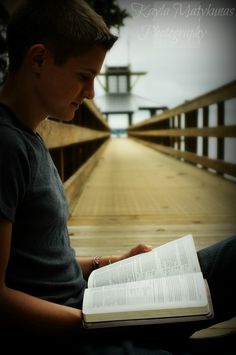 a young man sitting on the ground reading a book