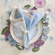 a table setting with napkins, wine glasses and flowers on the placemates