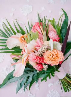 a bouquet of flowers is laying on a pink surface with leaves and flowers around it