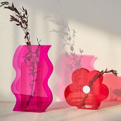 two vases with plants in them on a table next to each other, one pink and the other red