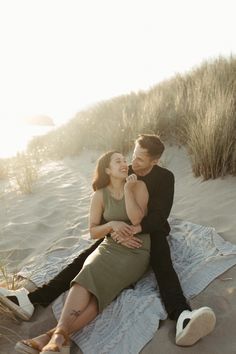 a man and woman sitting on top of a blanket in the sand