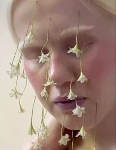 a woman with white flowers on her face and nose, covering her eyes from the sun