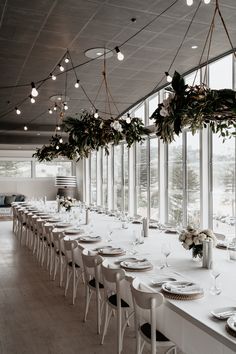 a long table with white plates and place settings in front of large windowed windows