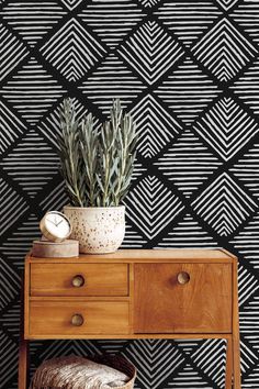 a wooden table with a potted plant on top of it next to a black and white wallpaper