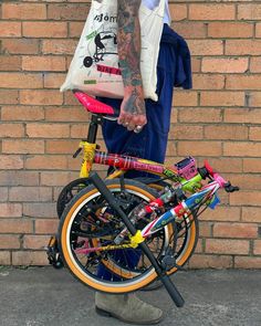 a man with tattoos on his arm standing next to a bike and carrying a bag