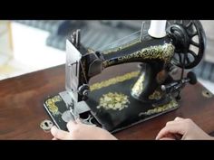 a woman is using a sewing machine to sew something on a wooden table in front of her