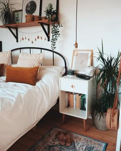 a bedroom with a bed, nightstand and potted plants