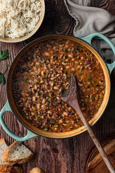 a pot filled with beans and rice on top of a wooden table next to bread