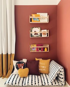 a day bed with bookshelves and pillows on it in front of a red wall