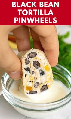 a person dipping some kind of food into a bowl with white cream and black bean tortilla pinwheels