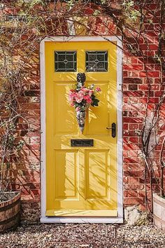 a yellow door with flowers on it in front of a red brick wall and potted plants