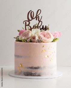 a pink cake with flowers and the word oh bake on top is sitting on a white table