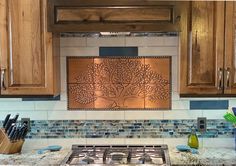 a kitchen with wooden cabinets and tile backsplash, stainless steel tree design over the stove