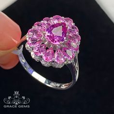 a person holding a pink ring with diamonds on it's sides and the center surrounded by smaller pink stones