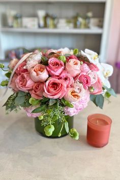 a vase filled with pink and white flowers next to a candle on a counter top