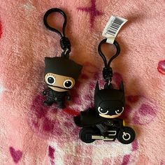 two key chains with batman and catwoman on them sitting on a pink blanket next to each other