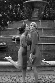 two women are kissing in front of a fountain