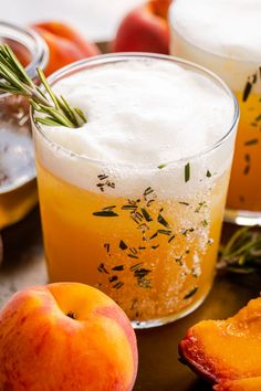 two glasses filled with drinks sitting next to peaches and other fruit on a table