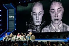 people sitting on chairs in front of a large screen with two men's faces