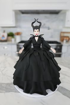 a doll is sitting on top of a counter in a black dress and devil horns