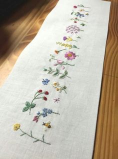 an embroidered table runner with flowers on the bottom and green stems in the middle, sitting on a wooden floor