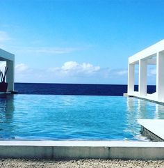 an empty swimming pool next to the ocean under a blue sky with white columns on it