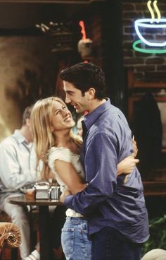 a man and woman hugging each other in front of a table with coffee cups on it