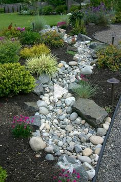 a garden with lots of rocks and flowers in the center, along side a house