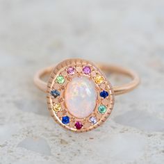 a white opal surrounded by multicolored stones in a rose gold ring on a marble surface