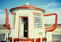 a red and white teapot shaped like a house on the beach with its door open