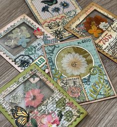 four cards with flowers and butterflies on them sitting on top of a wooden table next to each other