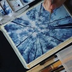 a person is drawing on a piece of paper with pencils and paintbrushes