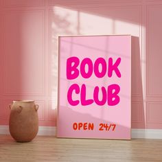 a pink book club sign sitting on top of a wooden floor next to a vase