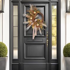 a black front door with a wreath on it and two potted plants next to it